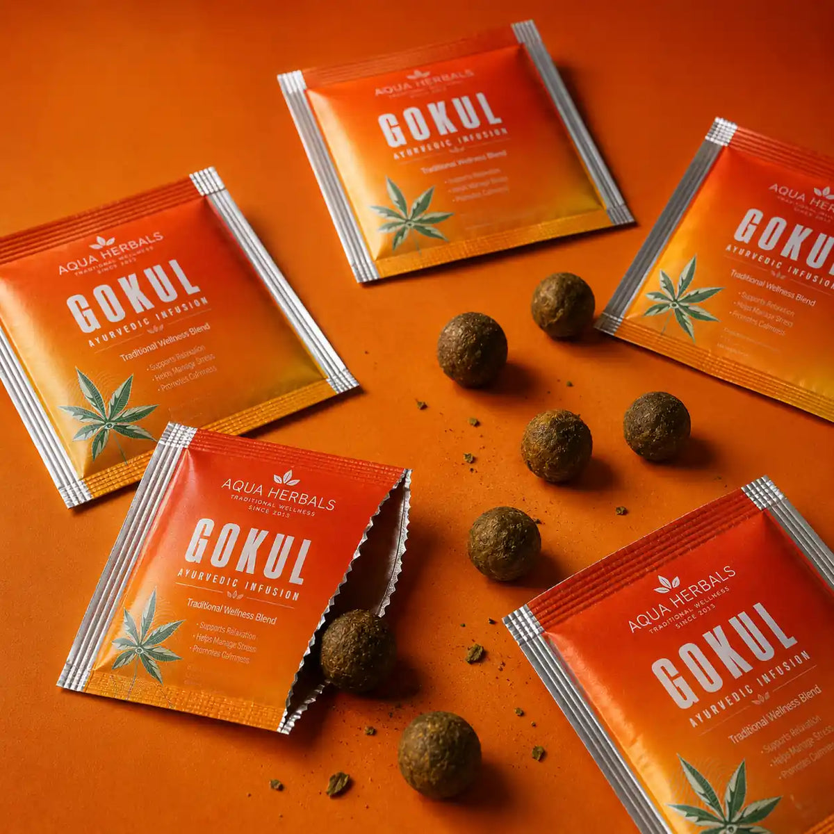 Aqua Herbals Gokul Ayurvedic Infusion premium sachets arranged with herbal wellness balls on an orange studio background